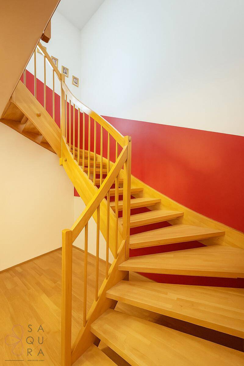 Helle Holztreppe mit Geländer, die zu den oberen Etagen führt, mit roter Wand.