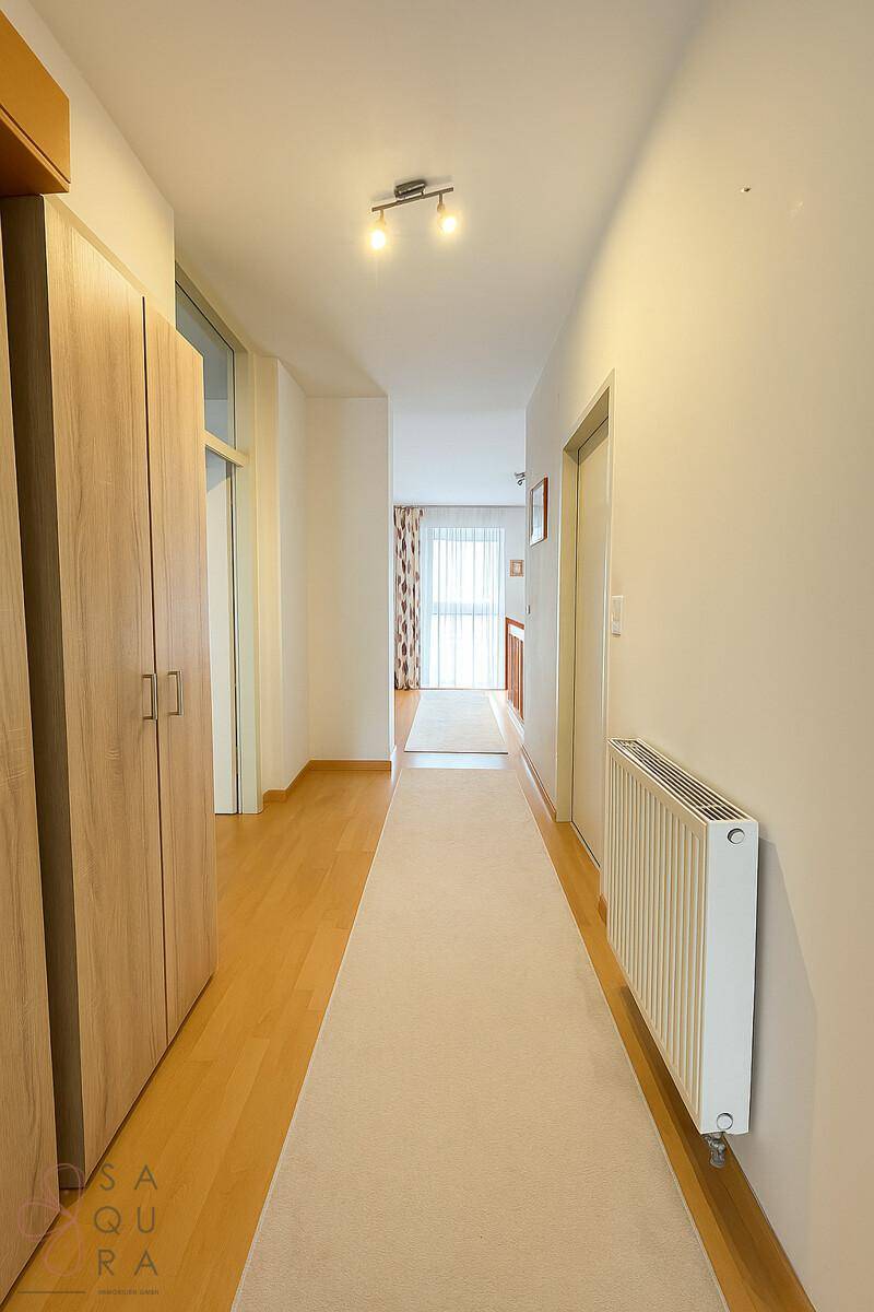 Langer, heller Flur mit Holzboden, Einbauschränken und Blick zum Fenster.