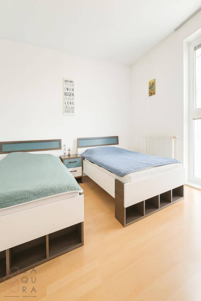 Helles Schlafzimmer mit zwei Einzelbetten, Holzboden und großem Fenster.