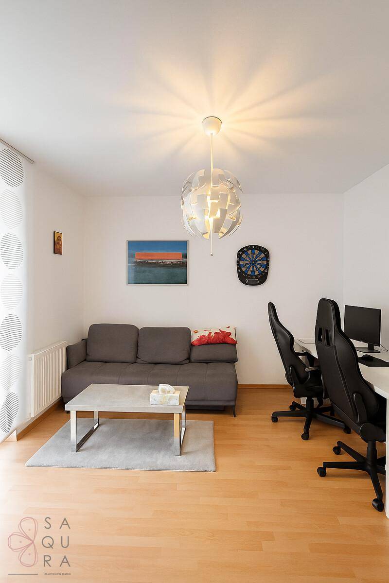 Heller Raum mit Sofa, Schreibtisch und modernem Deckenlicht, vielseitig nutzbar.