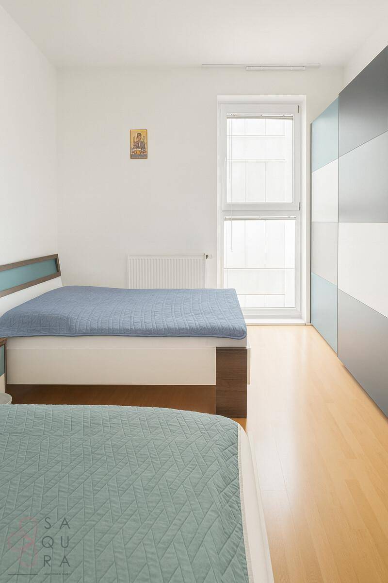 Schlafzimmer mit zwei Einzelbetten, Holzboden und großem Fenster mit viel Tageslicht.