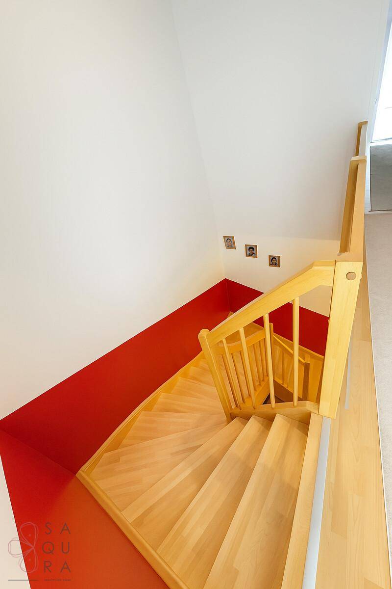 Blick von oben auf die helle Holztreppe mit roter Akzentwand und Holzboden.
