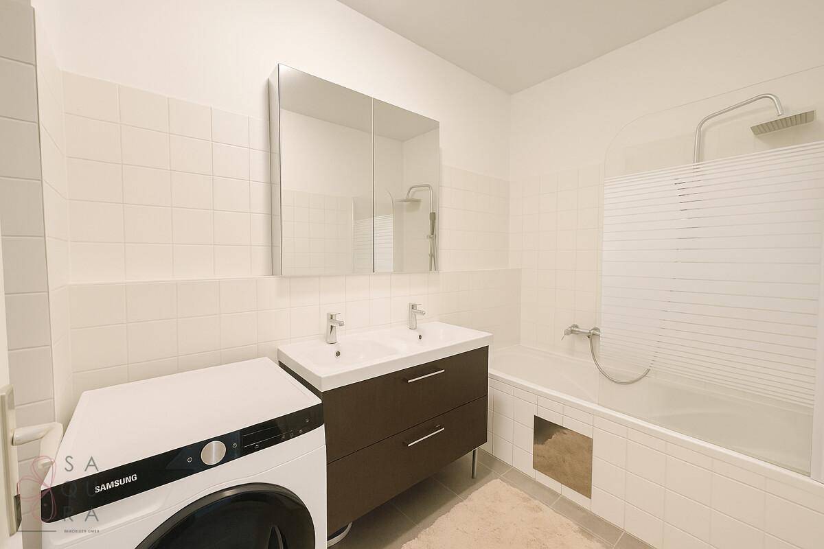 Helles Badezimmer mit Badewanne, Doppelwaschbecken und Waschmaschine.