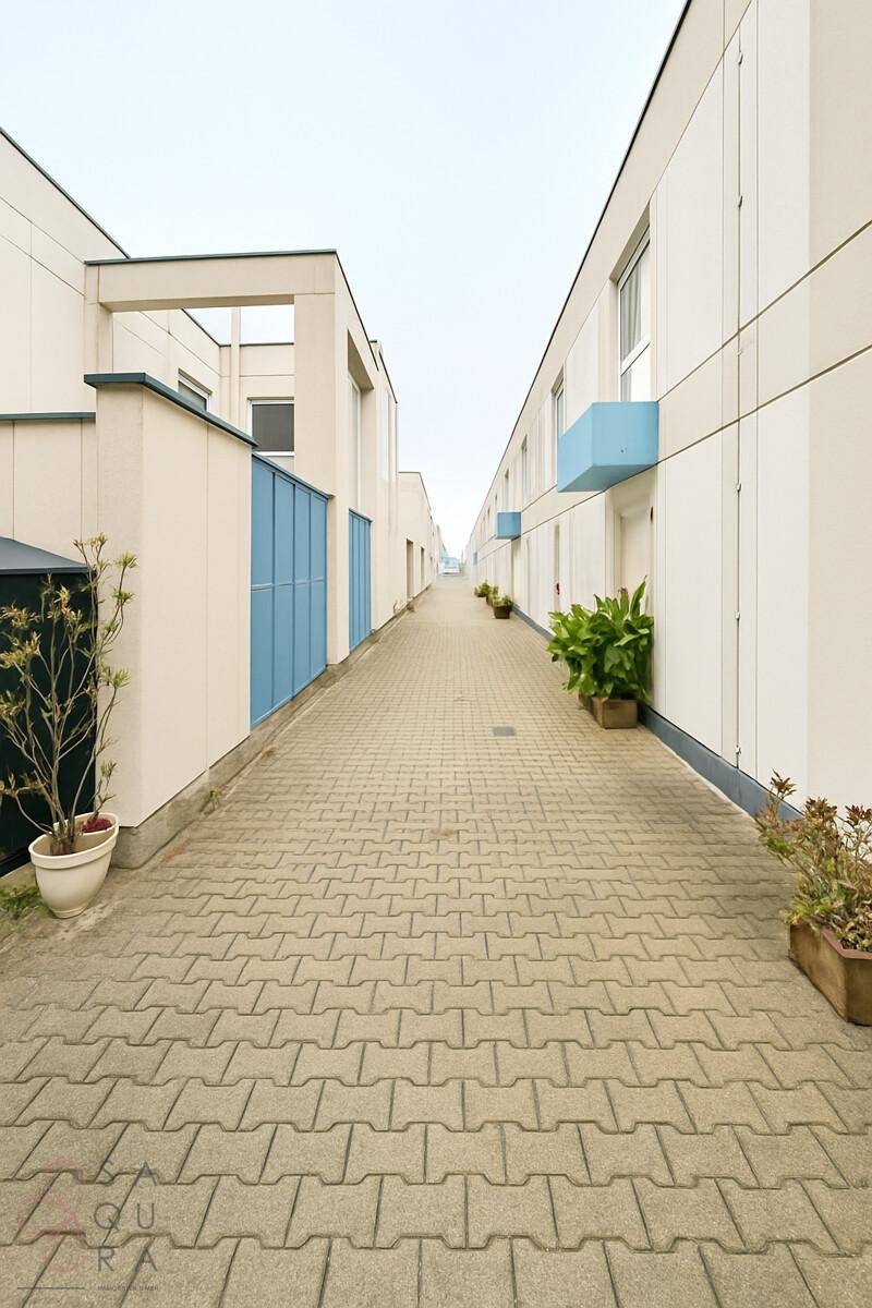 Langer gepflasterter Weg zwischen modernen Wohngebäuden mit blauen Akzenten.
