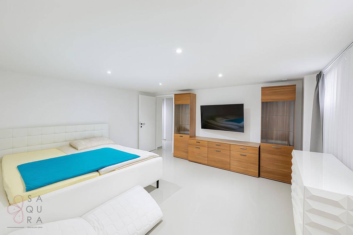 Helles Schlafzimmer mit weißem Bett, Holzmöbeln und einem Fernseher an der Wand.