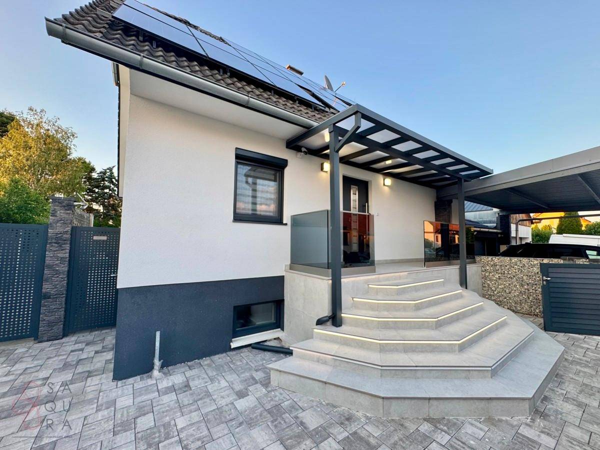 Modernes Einfamilienhaus mit Photovoltaikanlage auf dem Dach und beleuchtetem Eingangsbereich.