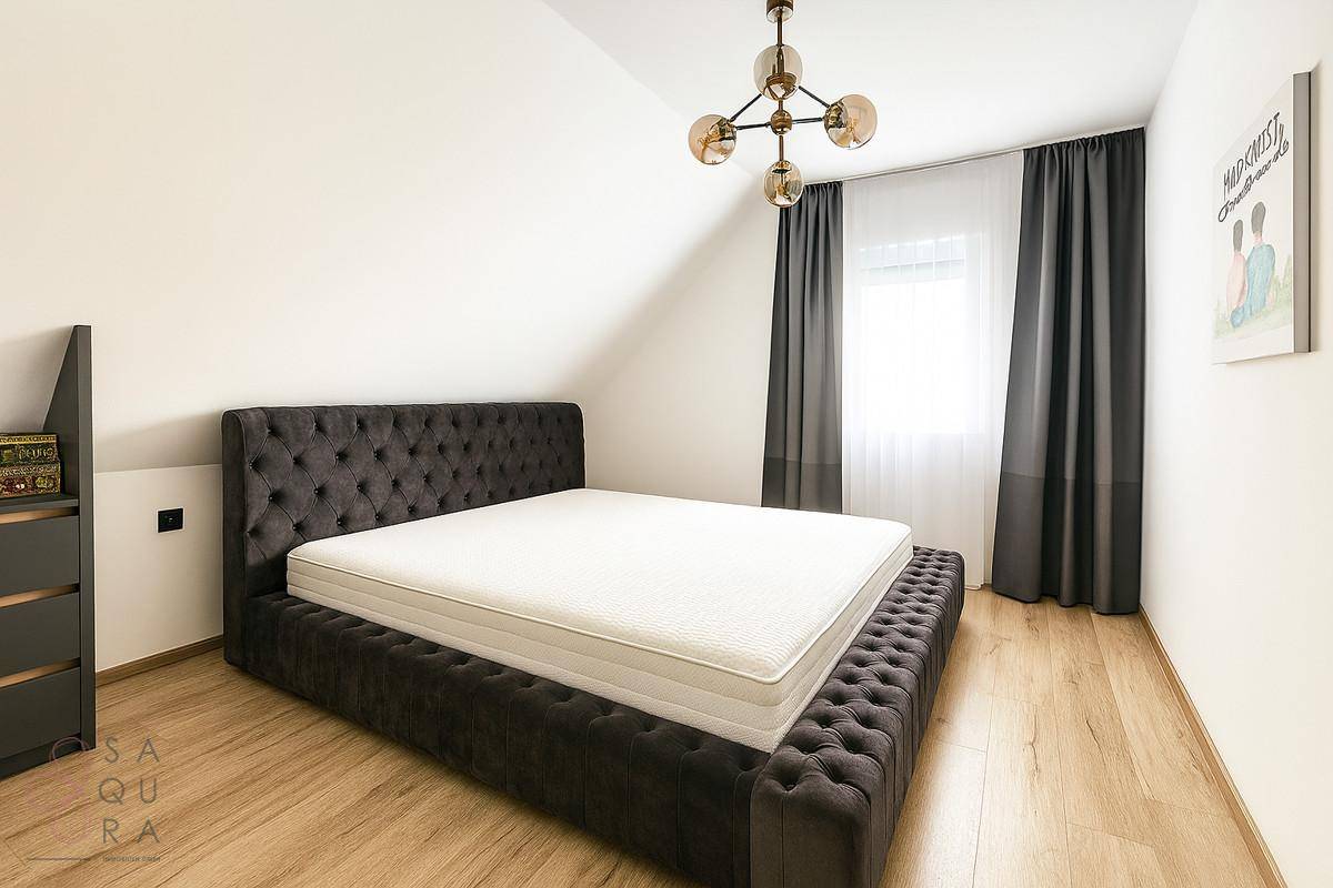 Gemütliches Schlafzimmer im Dachgeschoss mit dunklem Polsterbett und hellem Holzboden.