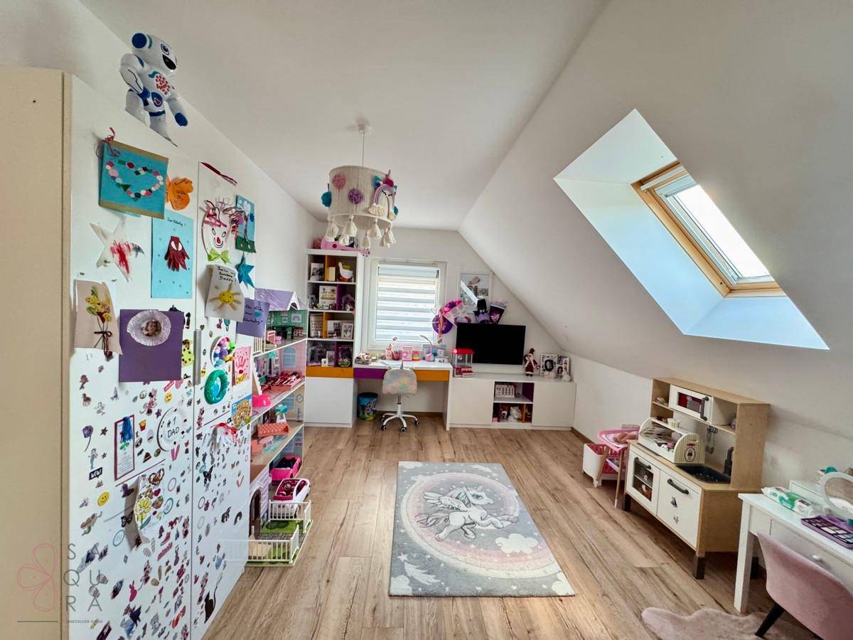 Geräumiges Kinderzimmer im Dachgeschoss mit Schreibtisch, Spielzeug und Dachfenster.