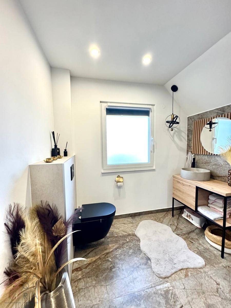 Modernes Badezimmer mit dunkler Toilette, Holzwaschtisch und Fenster für Tageslicht.