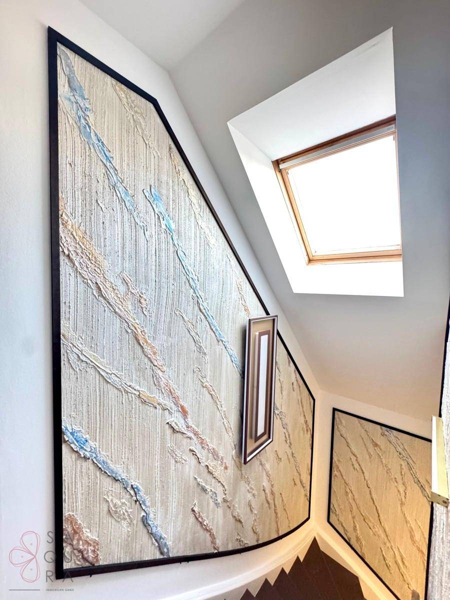 Treppenhaus mit künstlerischen Wandpaneelen und einem Dachfenster, das den Bereich erhellt.