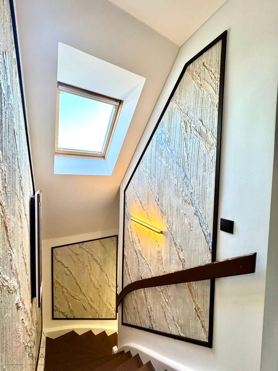 Treppenhaus mit modernem Design, dekorativen Wandpaneelen und einem Dachfenster für natürliches Licht.