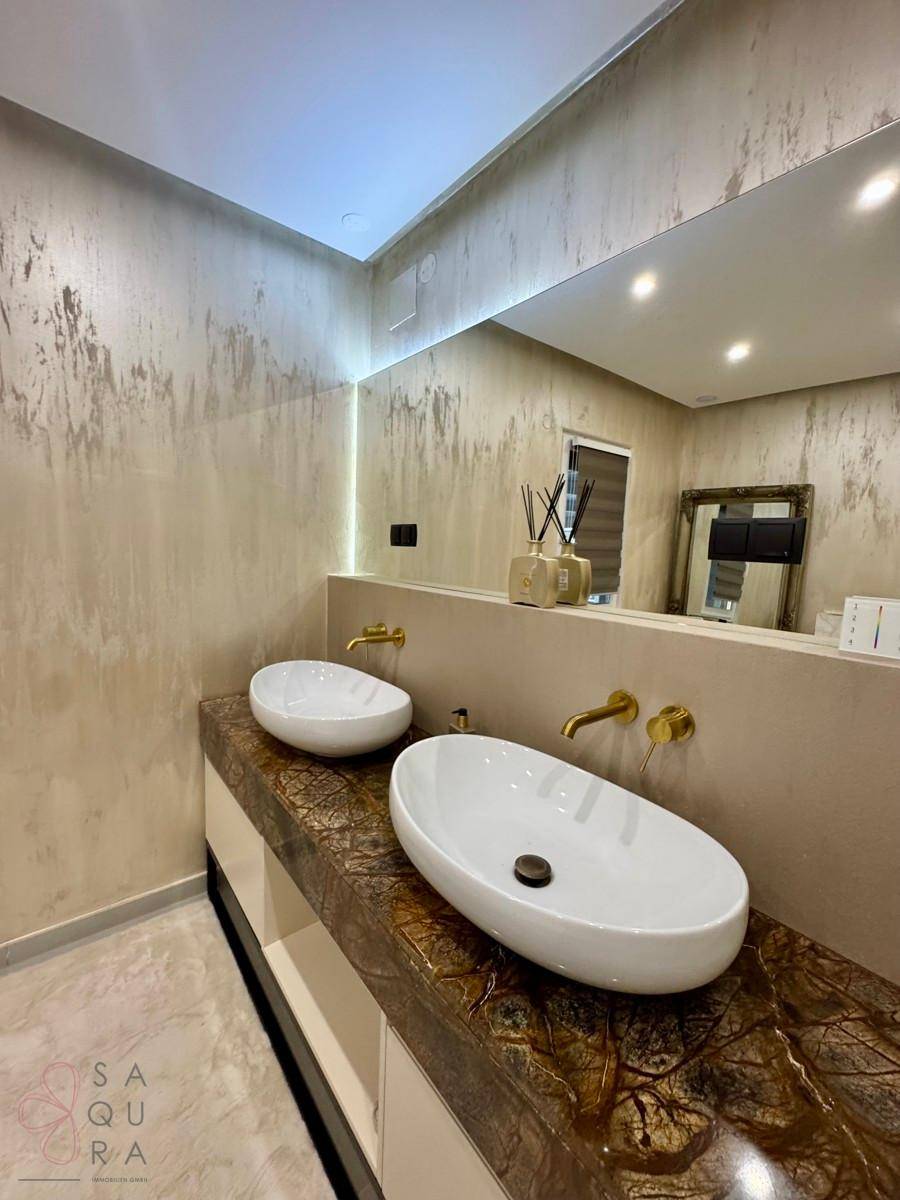Elegantes Badezimmer mit Doppelwaschbecken, goldenen Armaturen und einem großen Wandspiegel.