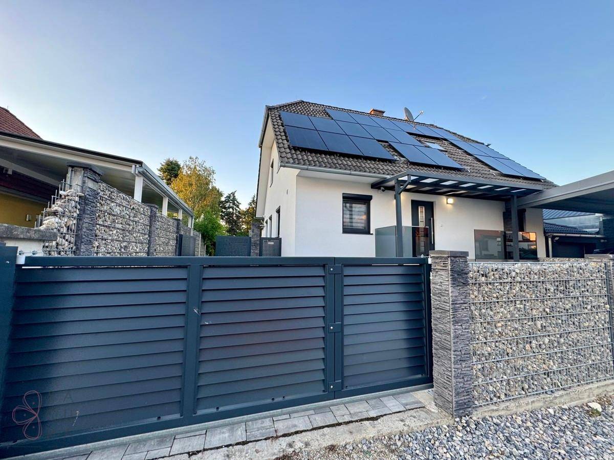 Hausfassade mit moderner Zaunanlage, Gabionen und Photovoltaikanlage auf dem Dach.