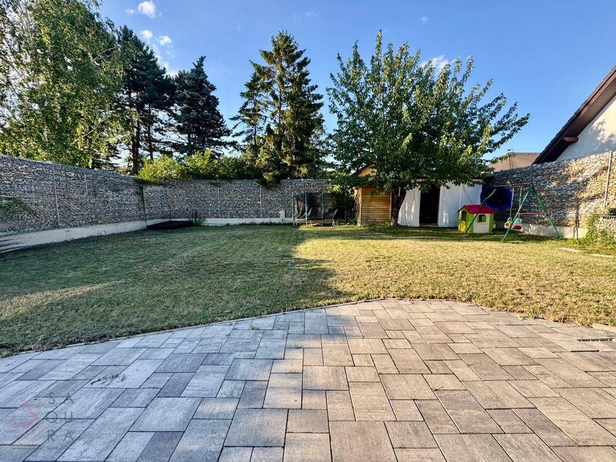 Großer Garten mit Rasenfläche, gepflasterter Terrasse und Kinderspielbereich im Hintergrund.