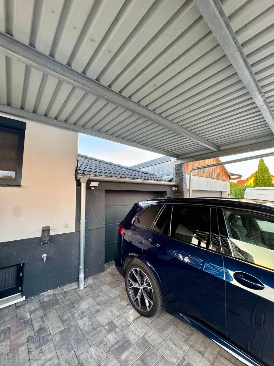 Überdachter Carport-Bereich neben dem Haus mit geparktem Auto und Garagentor.