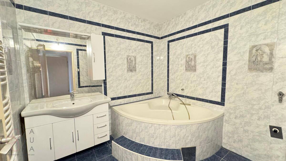 Badezimmer mit Eckbadewanne, blau-weißen Fliesen und einem Waschtisch mit Spiegel.