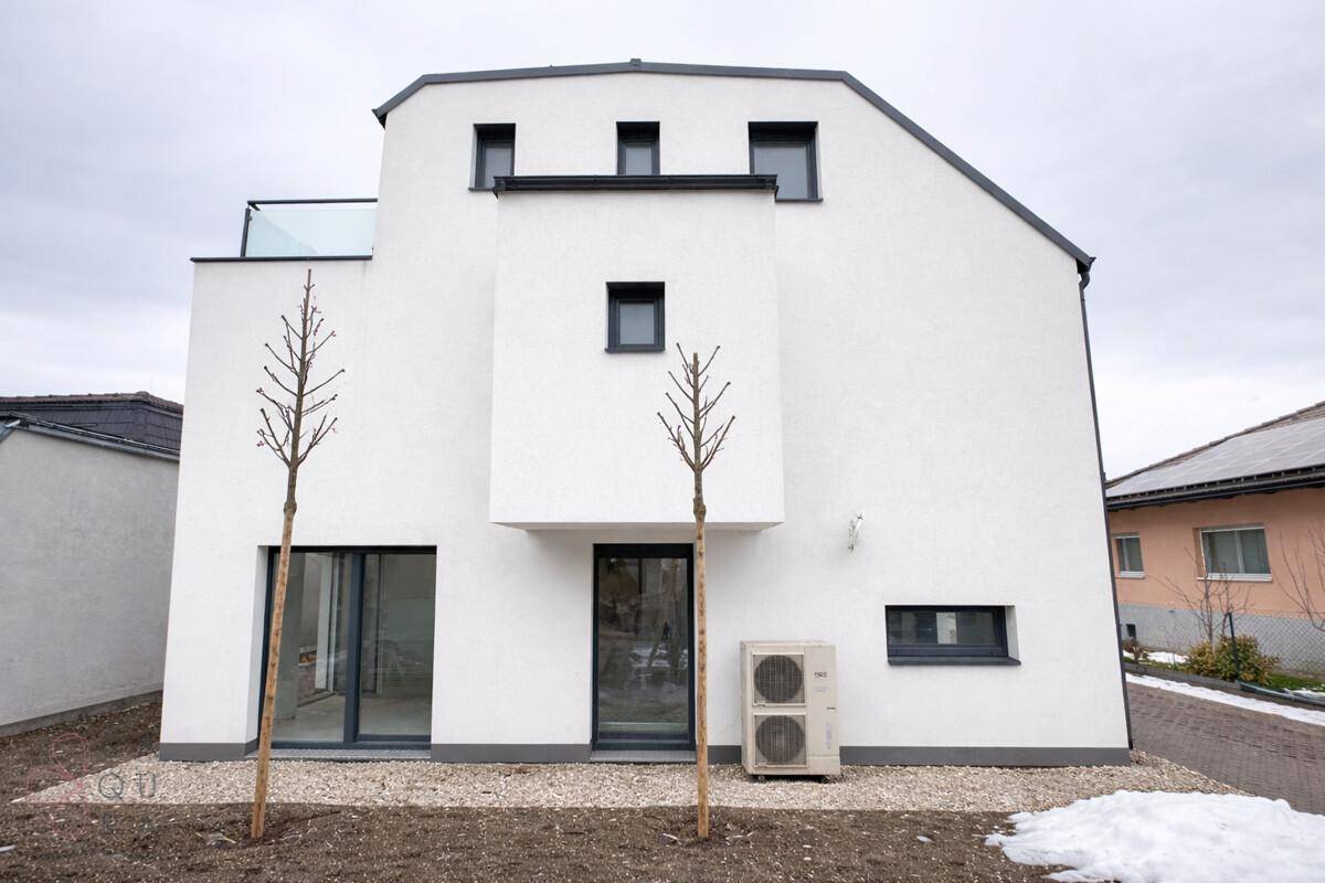 Vorderansicht eines modernen Reihenhauses mit weißer Fassade und Außeneinheit der Klimaanlage.