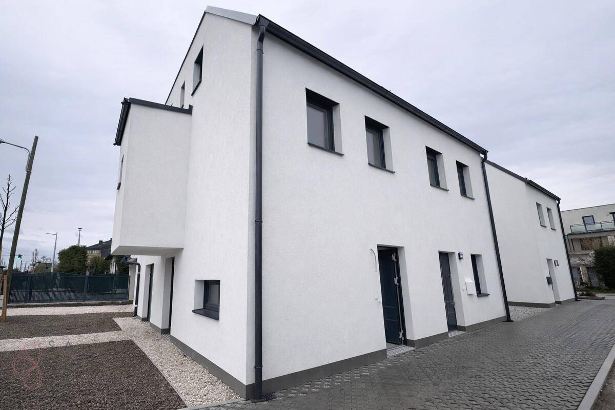 Seitenansicht eines neu errichteten Reihenhauses mit weißer Fassade und modernen Fenstern.