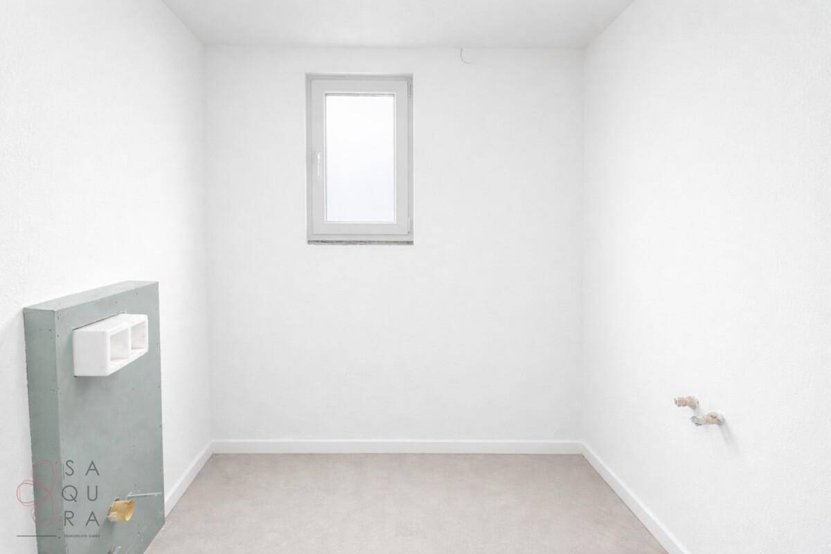 Leerer Raum mit Fenster und vorbereiteten Sanitärinstallationen für ein Badezimmer.