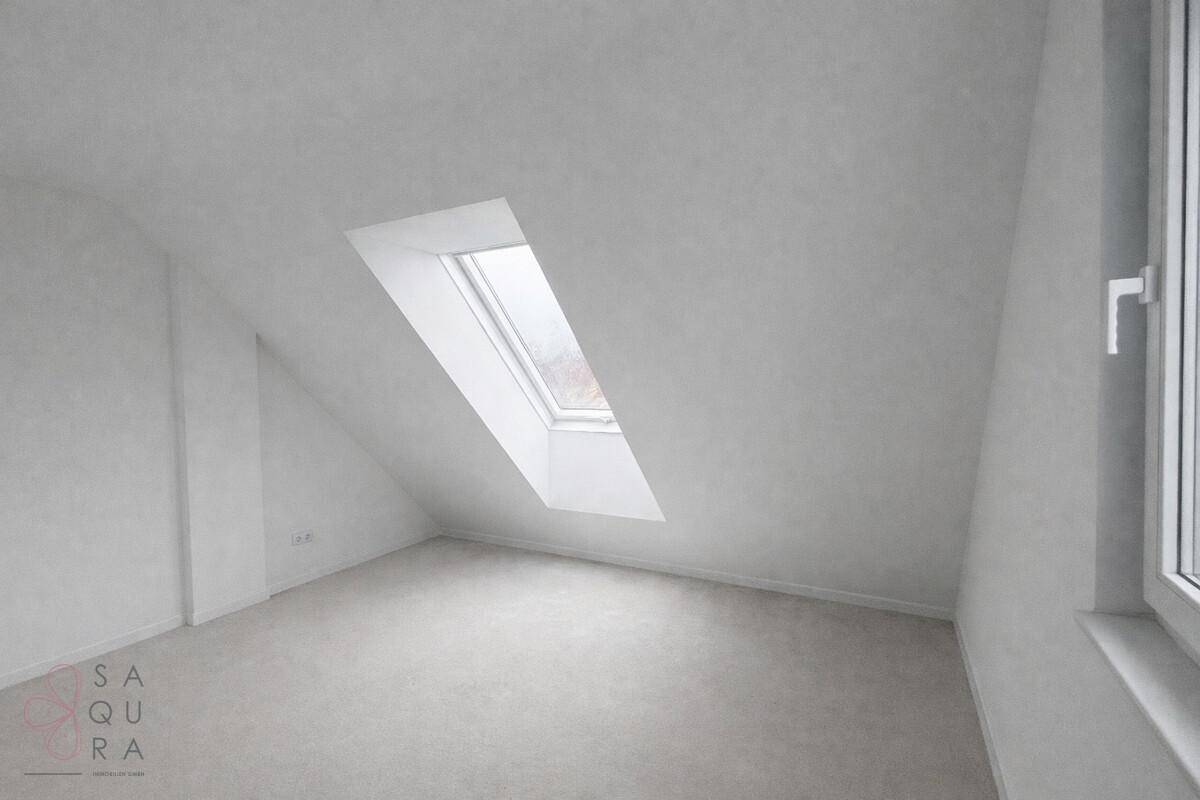 Dachzimmer mit schrägen Wänden und einem großen Dachfenster, bietet viel Tageslicht.