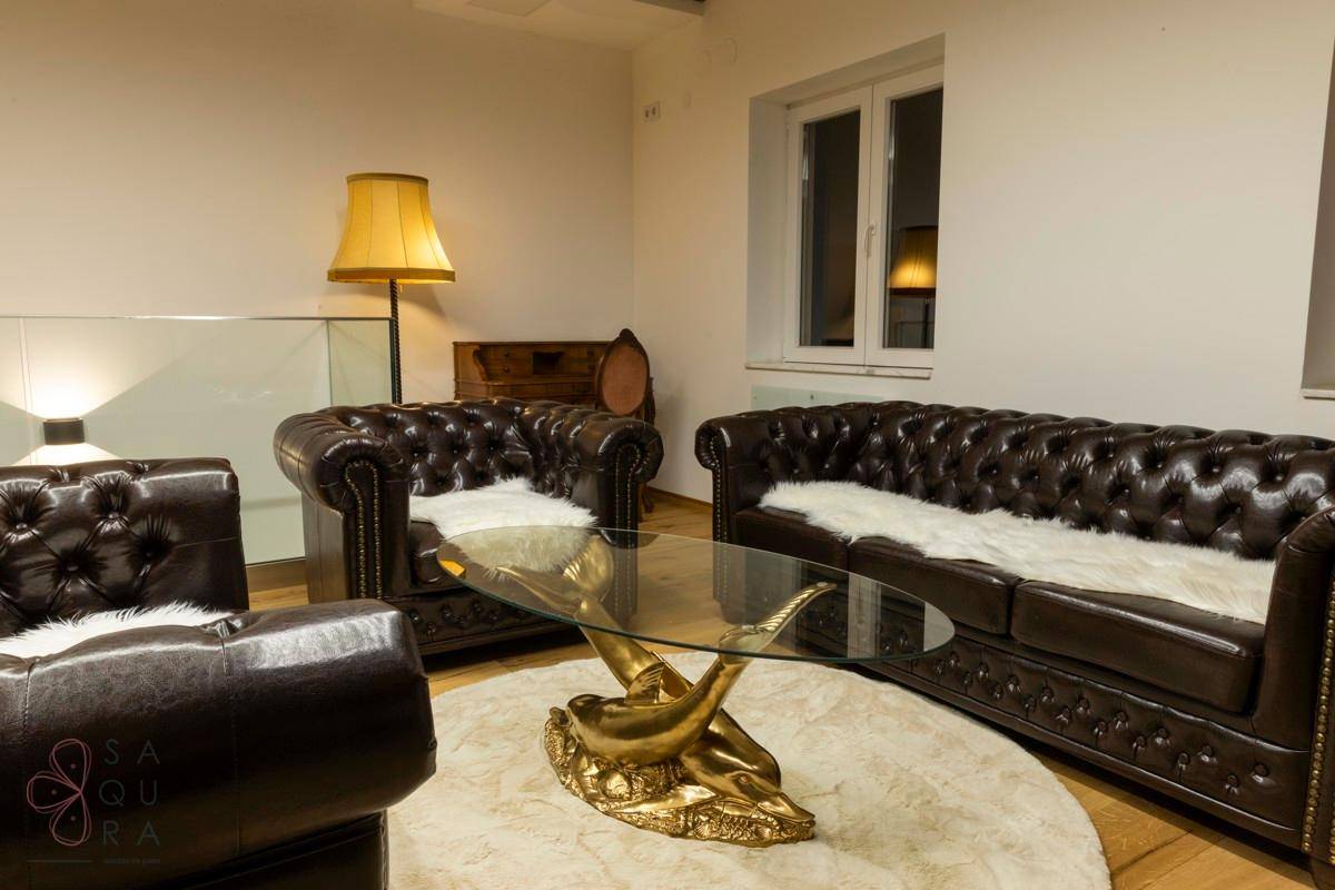 Wohnzimmer mit Chesterfield-Sofas, einem runden Teppich und einer auffälligen Couchtisch-Skulptur.