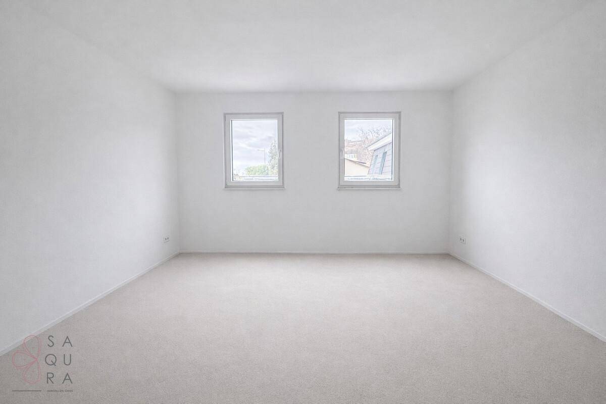 Helles, leeres Schlafzimmer mit zwei Fenstern und neutralem Estrichboden.