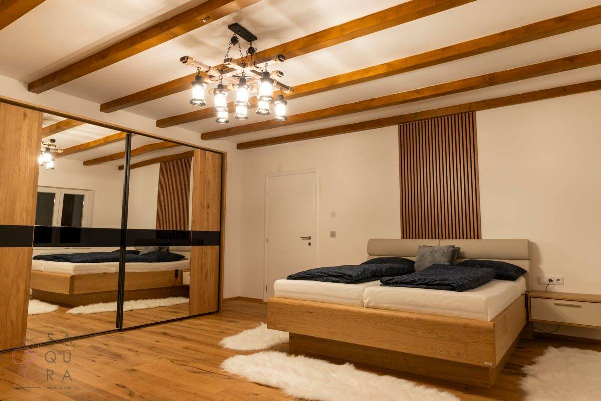 Schlafzimmer mit Holzbalkendecke, großem Bett und Spiegelschiebetürenschrank.