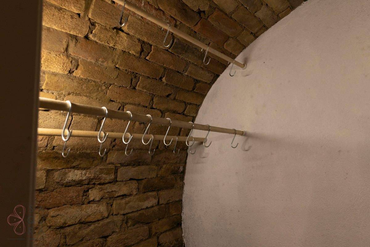 Detailansicht einer Ziegelwand im Gewölbekeller mit Holzstangen und Haken zur Aufbewahrung.