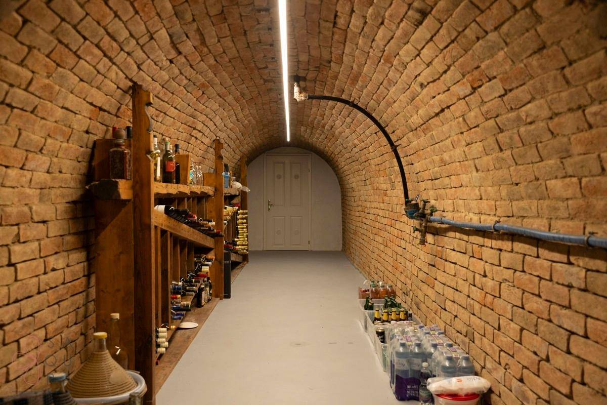 Ein langer Gewölbekeller mit Ziegelwänden, gefüllt mit Weinregalen und Getränkeflaschen.