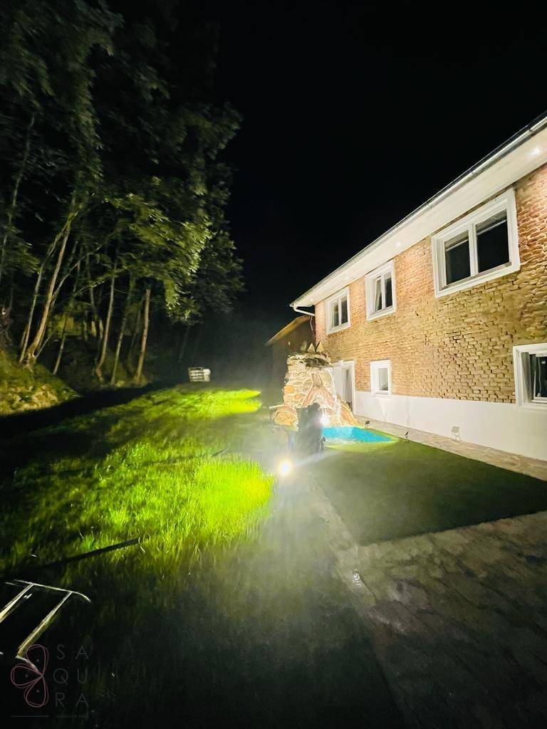 Ein beleuchteter Gartenbereich bei Nacht mit Rasen, Bäumen und einem Pool neben dem Haus.