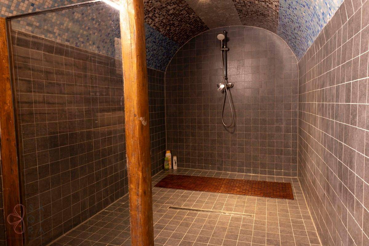 Eine geräumige begehbare Dusche mit dunklen Fliesen und Holzsäule in einem einzigartigen Badezimmer.