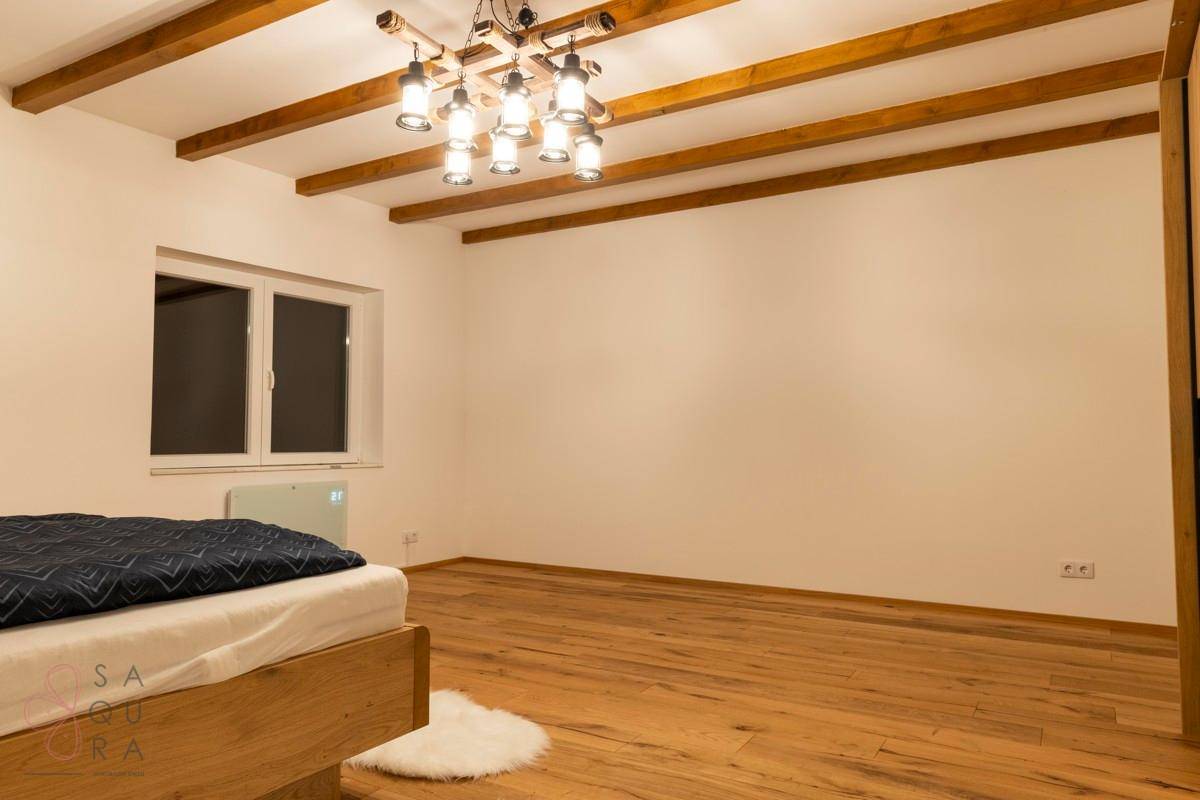 Ein geräumiges Schlafzimmer mit Holzboden, sichtbaren Deckenbalken und einem großen Fenster.