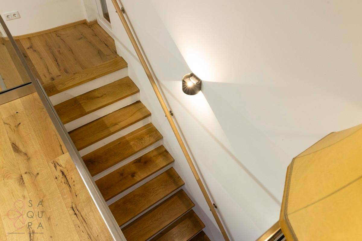 Eine moderne Holztreppe mit Glasgeländer führt in einen hellen Flur mit Holzboden.