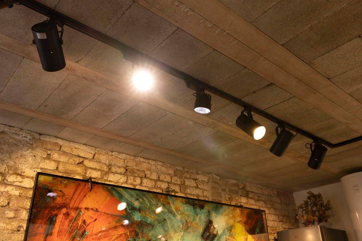 Deckenbeleuchtung mit Strahlern und Holzbalken über einem modernen Kunstwerk an der Wand.