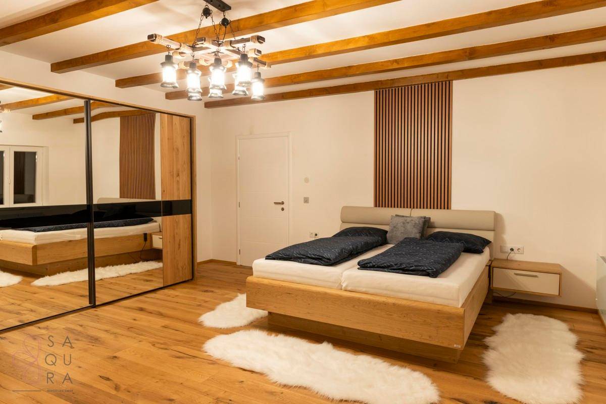 Ein modernes Schlafzimmer mit Doppelbett, Spiegelschrank, Holzboden und sichtbaren Deckenbalken.