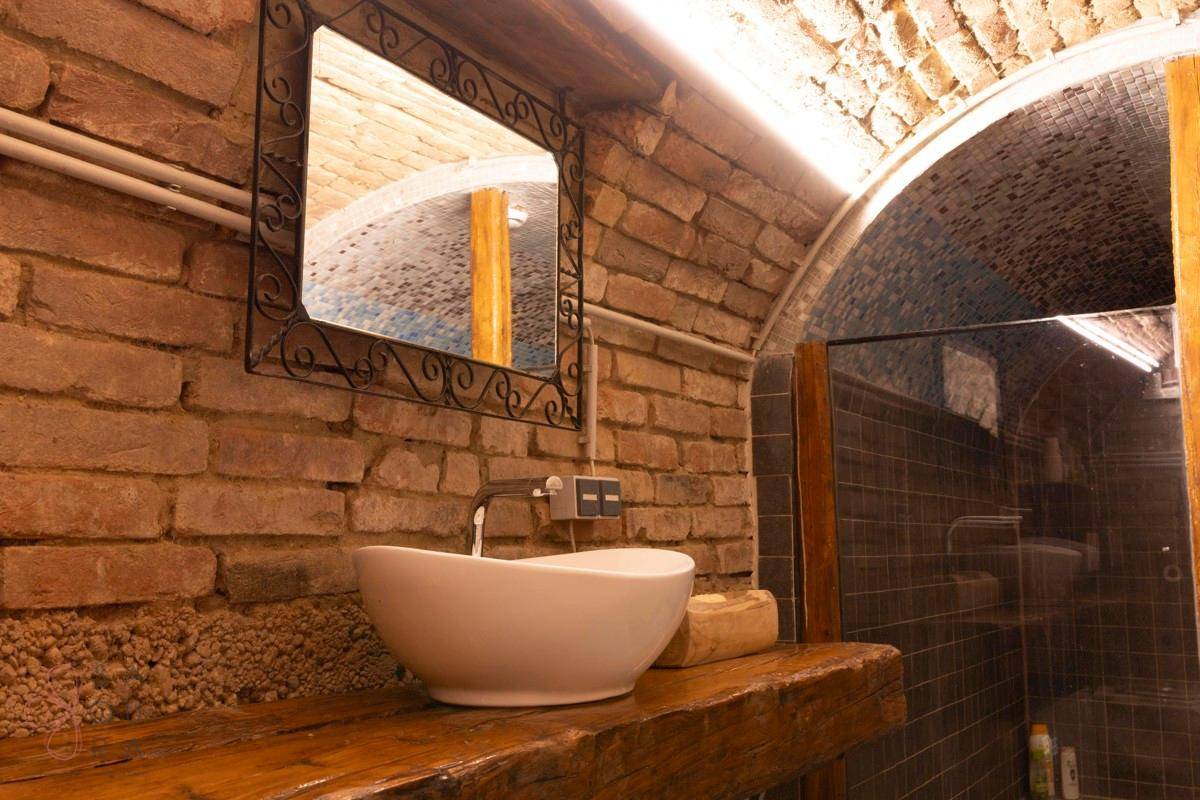 Nahaufnahme des Waschbeckens und Spiegels im rustikalen Badezimmer mit Ziegelwänden und Gewölbedecke.
