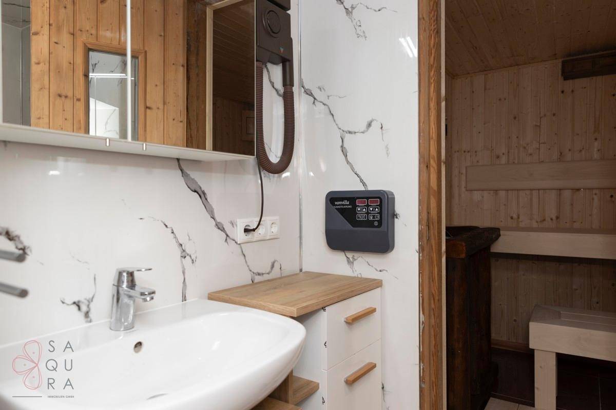 Modernes Badezimmer mit Marmoroptik-Fliesen, Waschbecken und Steuerung für die angrenzende Sauna.
