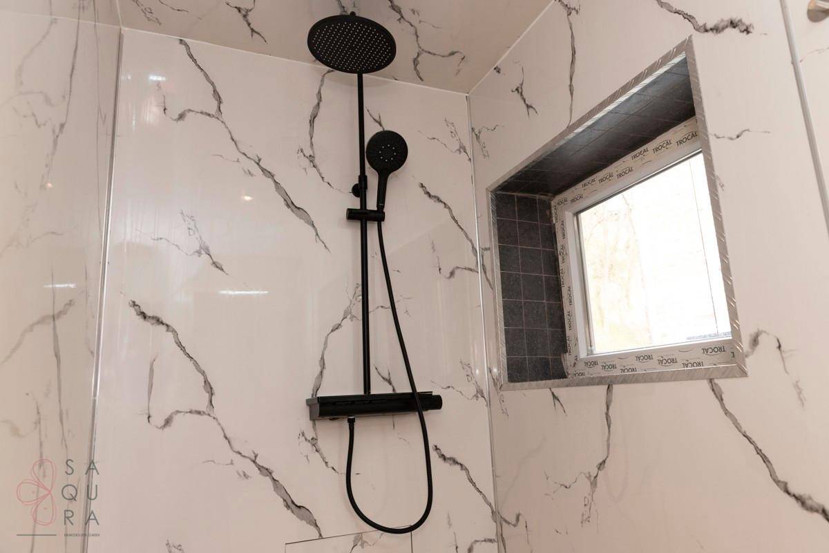 Moderne Dusche mit schwarzem Duschkopf, Marmoroptik-Fliesen und einem Fenster für Tageslicht.