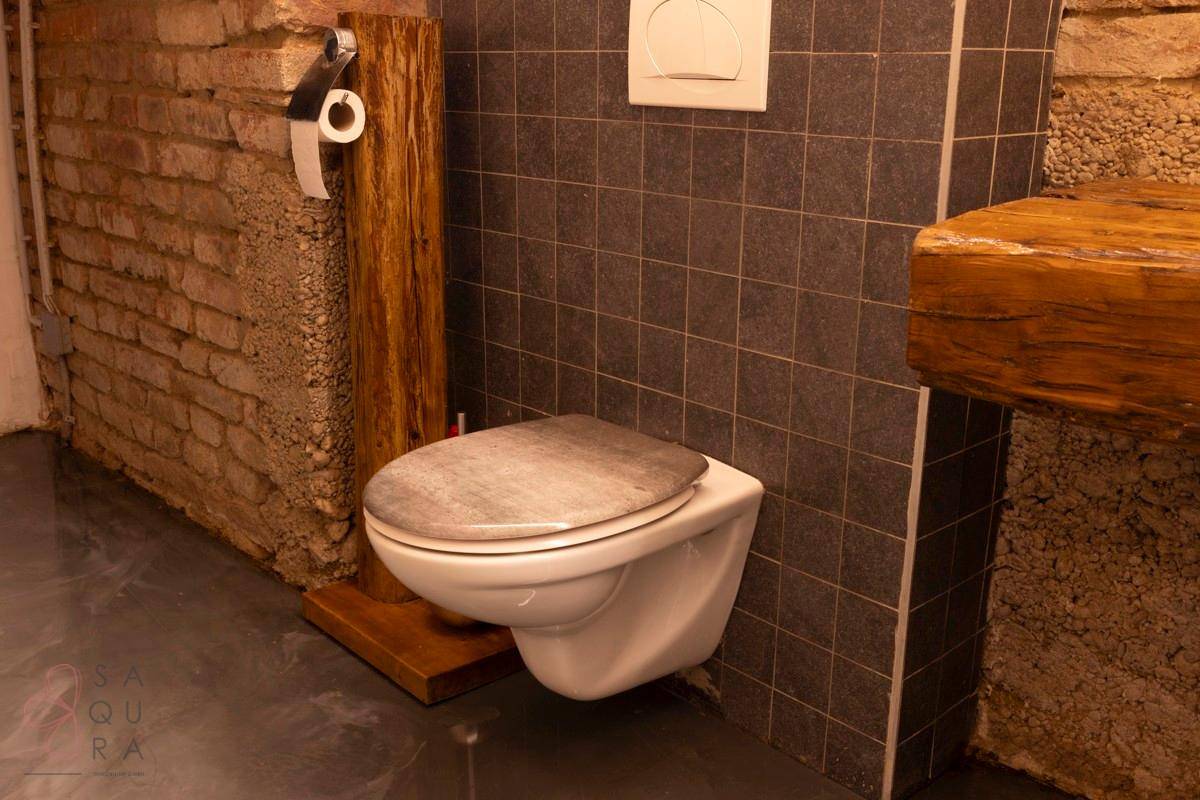 Wandhängende Toilette mit dunklen Fliesen und rustikalem Holzdetail in einem Kellerbadezimmer.