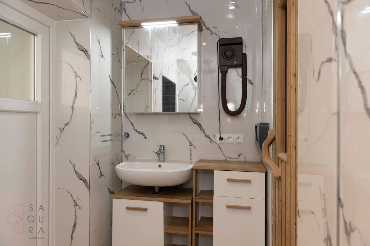 Helles Badezimmer mit Marmoroptik-Wänden, modernem Waschbecken und Zugang zur Holzsauna.