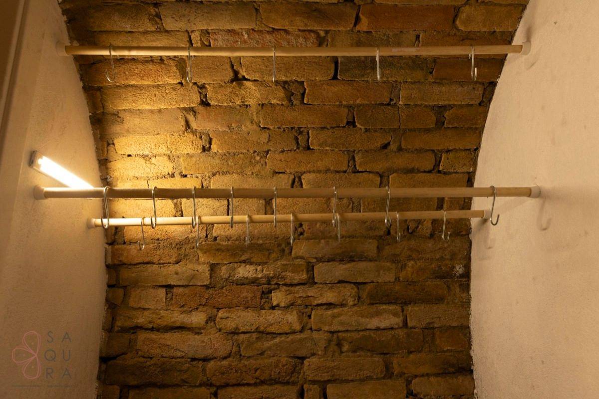 Rustikale Ziegelwand im Weinkeller mit Holzstangen und Metallhaken für verschiedene Utensilien.