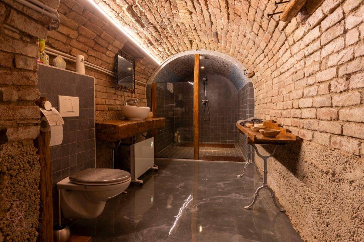Modernes Badezimmer in einem Gewölbekeller mit Ziegelwänden, Dusche und stilvollem Waschbecken.
