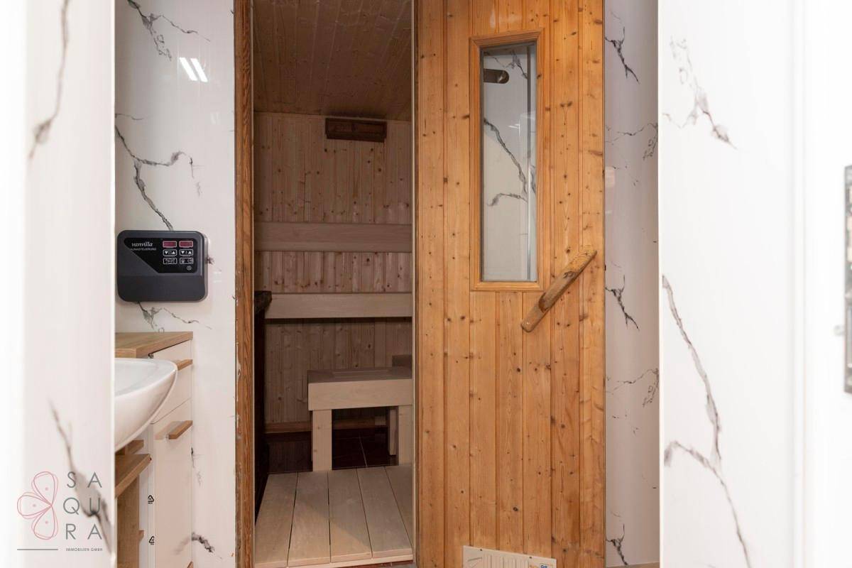 Blick vom Badezimmer auf die Holztür der Sauna, umgeben von Marmoroptik-Fliesen.