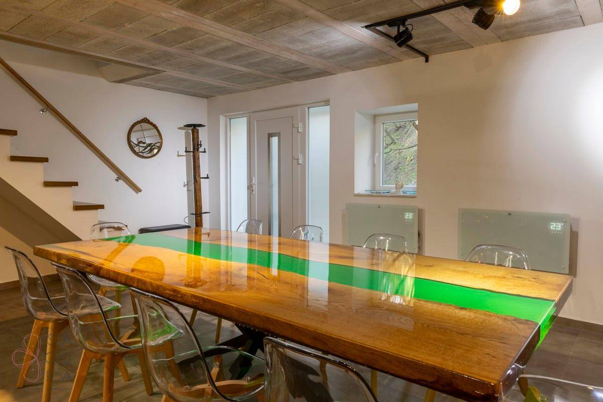 Ein großer Holztisch mit grüner Harzeinlage in einem offenen Wohnbereich mit Treppenzugang.