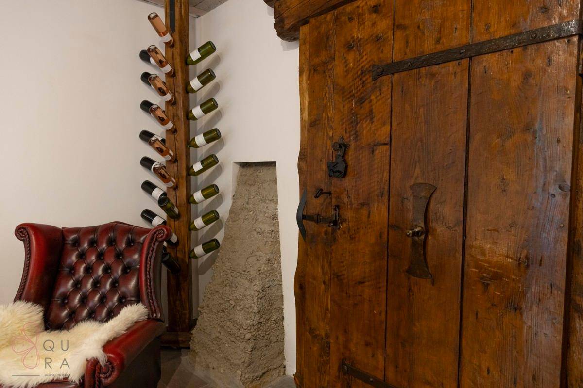 Ein antiker Ledersessel steht neben einem rustikalen Weinregal und einer massiven Holztür.