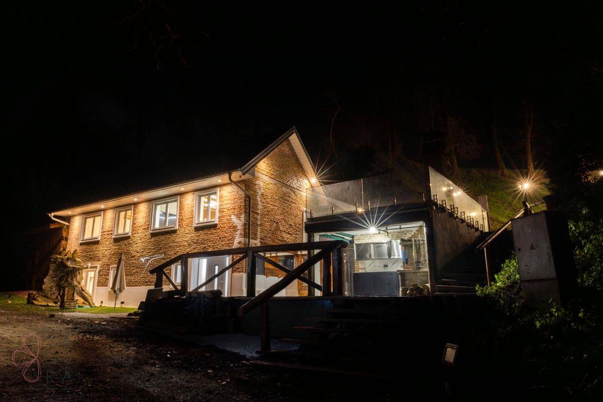 Beleuchtete Außenansicht des Hauses bei Nacht mit Terrasse und Außenküche.