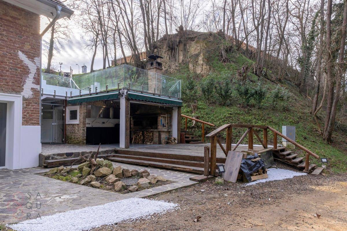 Weitläufiger Außenbereich mit Haus, Außenküche, Holzterrasse und Gartenanlage am Hang.