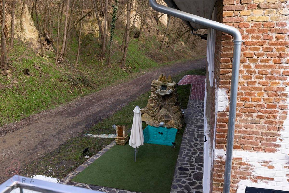 Gartenbereich mit Kunstrasen, Sonnenschirm und einem dekorativen Wasserbecken am Hang.