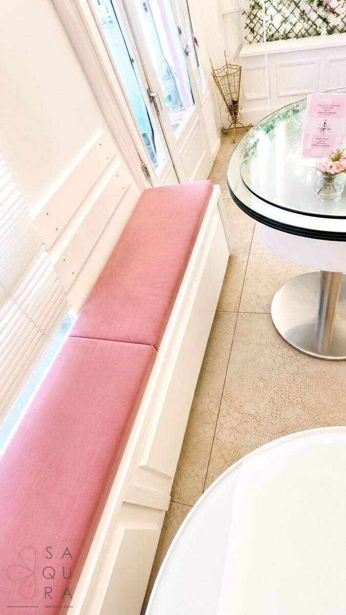 Gemütliche Sitzecke mit einer rosa gepolsterten Bank und einem runden Glastisch am Fenster.