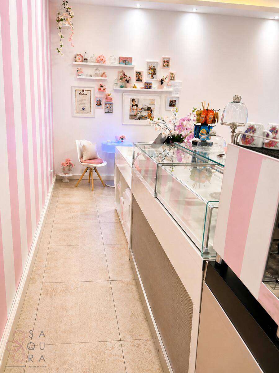 Schmaler Gang im Verkaufsraum mit einer Glasvitrine, gestreiften Wänden und dekorativen Regalen.